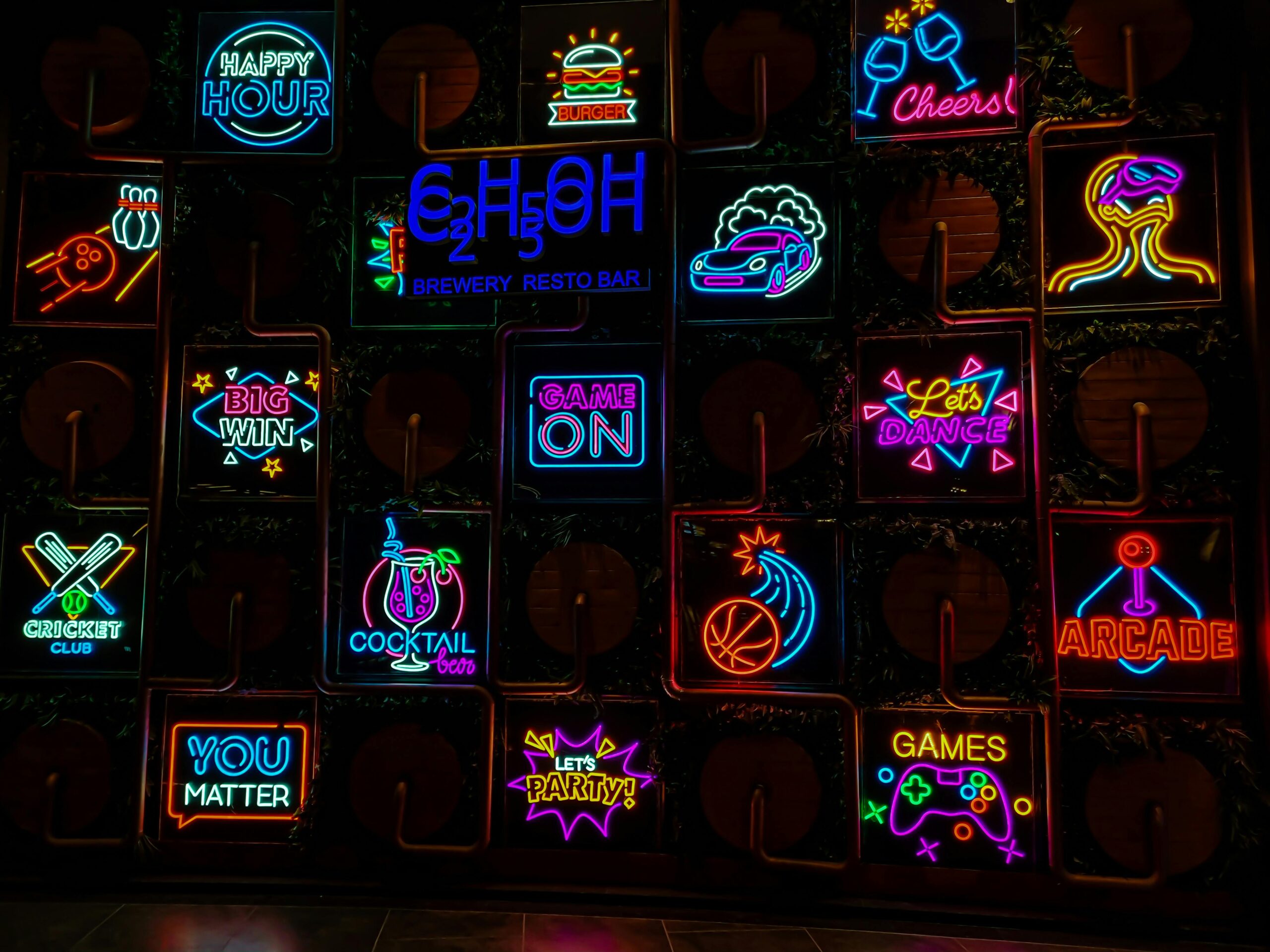 Vivid neon signs showcasing cocktails, gaming, and nightlife at a Gurugram bar.